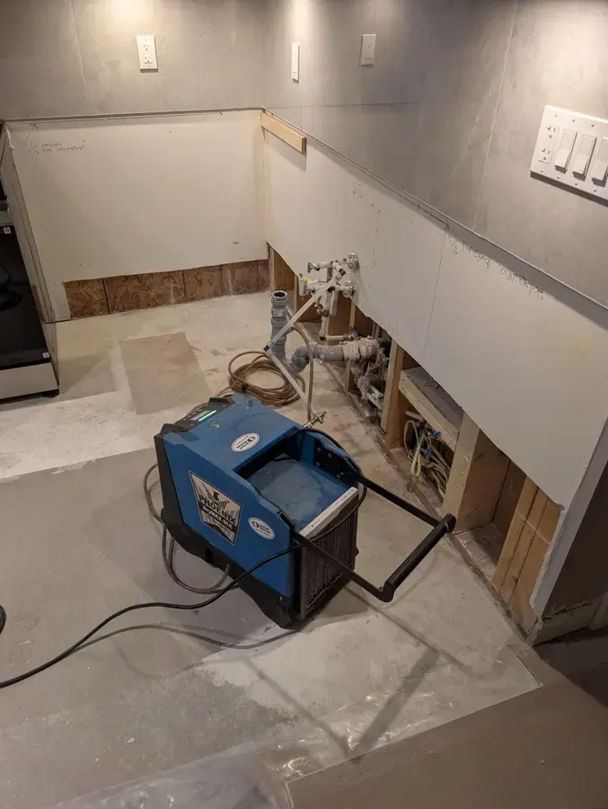 Kitchen with lower drywall removed and a dehumidifier running after a leak